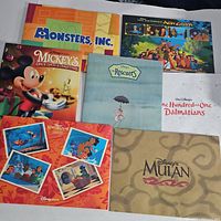 Top view showing assorted Disney lithographs with artwork from 'Monsters, Inc.', 'Mickey's Once Upon A Christmas', 'The Emperor's New Groove', 'The Rescuers', '101 Dalmatians', and 'Mulan'.