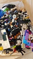 Mixed pile of various LEGO pieces including bricks, plates, and some minifigure parts, showing different colors and shapes for building sets.