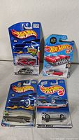 Four Hot Wheels cars in original packaging displayed on a white surface, showing the variety of models.