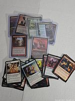 Overview of a stack of Magic The Gathering cards in plastic sleeves and some unsleeved laid out, showing varied card backs and fronts.