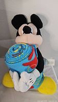 Front angle of Mickey Mouse plush holding the rolled throw blanket showing vibrant colors and soft plush materials