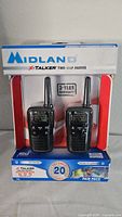 Front view of original packaging showing two Midland X-Talker two-way radios with antennas, display screens, and control buttons.
