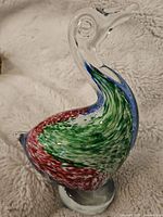 Full view of the Murano style glass figurine showing the curved neck and multicolor speckled body in green, red, and blue with clear glass base.
