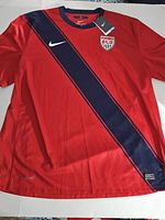 Red Nike Dri-Fit U.S. Soccer jersey size 2XL with tags, front view showing diagonal navy stripe, team crest, and Nike logo.