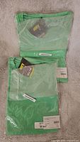 Two folded green Wingtech women's shirts in packaging, showing the size and color tags.