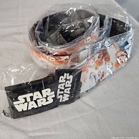 Overall view of the rolled Star Wars belt in plastic packaging showing part of the buckle and belt graphics.