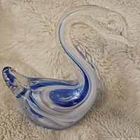 Front view of the vintage clear and blue swirled glass swan figurine on a soft beige fabric background.