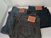 Three pairs of folded Levi's jeans in black, dark blue and light blue denim shown from back pockets and waistband area with Levi's branded patch and red tabs.