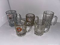 Five A&W glass mugs of varying sizes with different logos placed on white surface