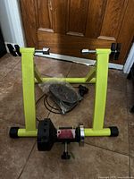 New bright yellow bicycle trainer stand with adjustable clamps and resistance unit attached, includes control cable and instruction manual.