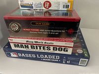 Stack of four sealed board games showing titles and box designs including NHL Hockey Night, Man Bites Dog, Bases Loaded, and Blockbuster