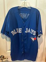 Front view of the blue Toronto Blue Jays jersey with team logo and name, showing buttons and neckline.