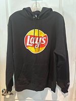 Black Champion hoodie, front view showing large Lays logo in red, yellow and white on chest, hoodie hanging on hanger