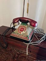 Front-angle view showing red and silver handset, rotary dial with Coca Cola logo, and base with Coca Cola branding and decorative green and red tiles.