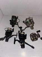 Four fishing reels laid on a white surface, showing various angles highlighting reels and grips.