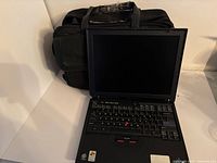 IBM ThinkPad laptop open with screen visible, black carrying bag behind.