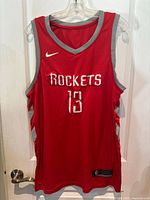 Front view of red Houston Rockets basketball jersey with number 13 and Nike swoosh logo.