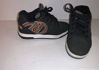 Side and top views of black Heelys athletic shoe with orange logo showing condition and design details.