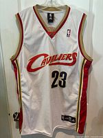 Front view of white sleeveless Cleveland Cavaliers jersey with LeBron James #23, features team logo and Adidas branding.