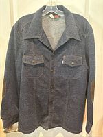 Front view of dark blue Levi's denim jacket with elbow patches, hanging on clear plastic hanger against white background.