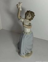 Front view of the porcelain figurine showing the girl holding the dove bird on her outstretched right hand, wearing a blue skirt and white blouse.