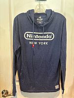 Front view of navy blue Nintendo New York hoodie hanging on a hanger, showing the main logo and design