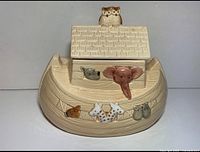 Front view showing the Noah's Ark shaped ceramic cookie jar with multiple animal figures painted on the front side and the owl on the roof lid.