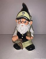 Front view of the Pittsburgh Penguins garden gnome coin bank showing the gnome holding a mug and a wooden sign reading 'PENGUINS GOLD'. The gnome wears a cream-colored Pittsburgh Penguins cap with logo and has a white beard.