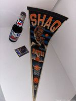 Image of Shaquille O'Neal pennant showing cartoon image of Shaq dunking and text 'SHAQ RATTLE THE RIM' with basketball hoop graphic.
