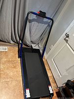 Full view of the treadmill showing the running belt and foldable frame with black and blue colors, safety cord hanging on the handle.