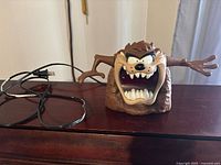 Front view of Tasmanian Devil clock showing face, mouth open and arms extended, with power cord visible behind.