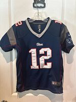 Front view of navy blue New England Patriots youth jersey with number 12 and Tom Brady association