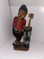 Front view of the hand-carved wooden golfer statue showing detailed facial features, clothing, and golf bag with clubs.