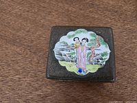 lid view showing figural enamel scene and engraved metal surface