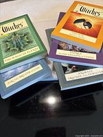 Stack of multiple themed Witches' Almanac paperback issues in blue, green, orange, purple plus spiral-bound book