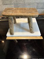 Overall view of stool showing rectangular seat, two legs, ruler for scale