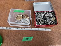 Two containers side by side, showing keychains in red tin and assorted items in clear box with tape measure for scale