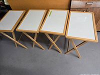 Four folding tray tables opened, showing white tops and wood frames