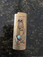 Front view showing owl motif and turquoise cabochon on brass lighter holder