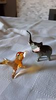 Photo of miniature amber glass dog figurine and small gray elephant figurine on a white textured fabric surface under natural light.