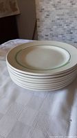Stack of eight cream/off-white 10-inch dinner plates with thin green and black stripes near the rim.
