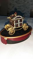 Front and side view of the gold-colored ornamental carriage trinket box with multicolored stones on black velvet display plinth