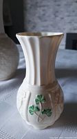 Short Belleek porcelain vase with flared top, vertical ridges, and embossed green shamrocks on the lower bulbous portion