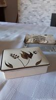 Photo showing two small vintage decorative boxes; one ceramic with brown floral design on lid, one glass with ornate metal lid showing tarnish.