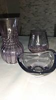 Three glass items displayed: two vintage amethyst glass vases of different heights and a modern art glass bowl with amethyst hues.