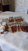 Group photo showing all cutlery items arranged on a white patterned tablecloth including forks and knives with brown Bakelite handles.