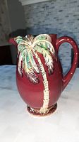 Front view of a vintage Beswick ceramic jug in deep red with palm tree decoration.