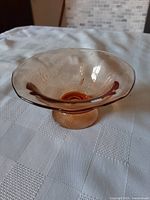 Photo of the amber glass bowl showing the full shape, pedestal base, and flared rim on a white tablecloth.