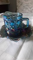 Photo showing the blue iridescent carnival glass creamer on matching dish, highlighting iridescent color and patterning