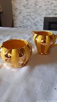 Photo of creamer and sugar bowl set showing yellow and gold striped glossy finish and rounded shape.